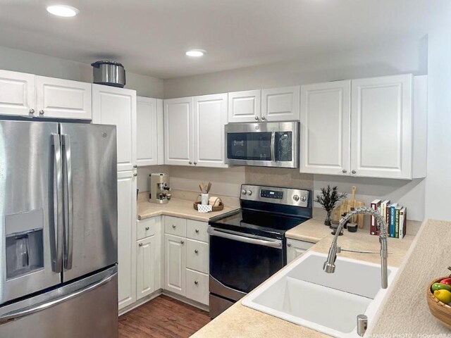 kitchen with appliances with stainless steel finishes, dark hardwood / wood-style floors, sink, and white cabinets