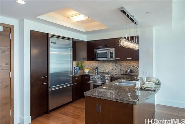 kitchen with sink, hanging light fixtures, dark brown cabinets, high quality appliances, and a raised ceiling