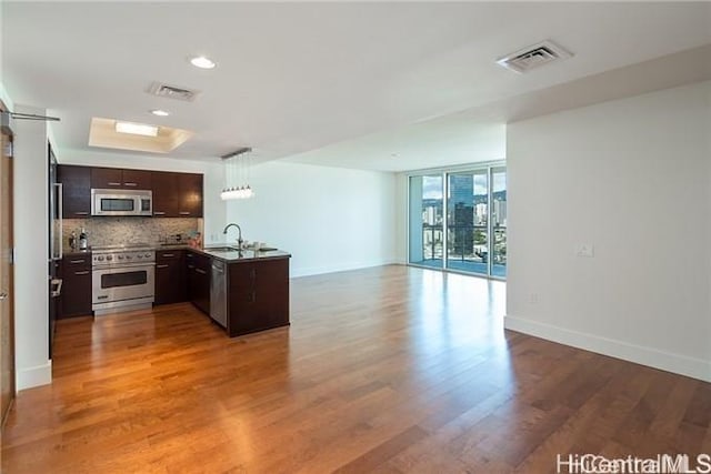 kitchen featuring appliances with stainless steel finishes, hardwood / wood-style floors, dark brown cabinetry, tasteful backsplash, and kitchen peninsula