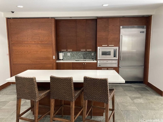 kitchen with built in appliances, a breakfast bar, sink, and backsplash