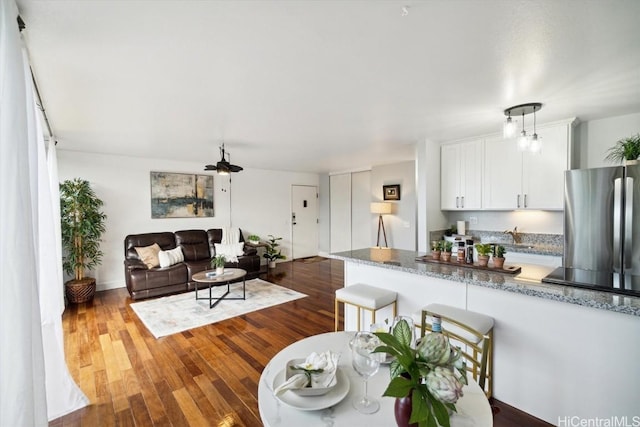 kitchen featuring dark wood-type flooring, a kitchen bar, white cabinetry, light stone counters, and stainless steel refrigerator