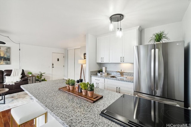 kitchen featuring hardwood / wood-style floors, stainless steel refrigerator, sink, white cabinets, and light stone countertops