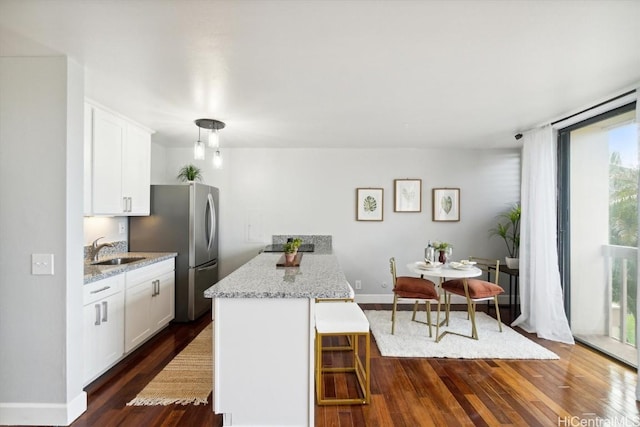 kitchen with stainless steel fridge, a breakfast bar area, white cabinetry, light stone countertops, and dark hardwood / wood-style flooring