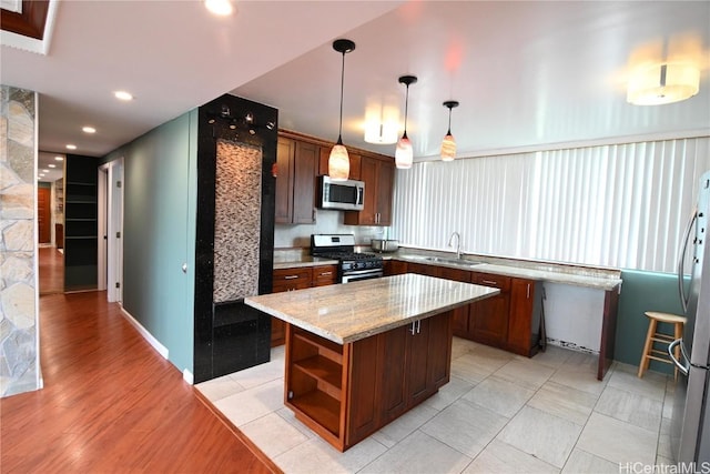 kitchen with pendant lighting, sink, stainless steel appliances, a center island, and light stone counters