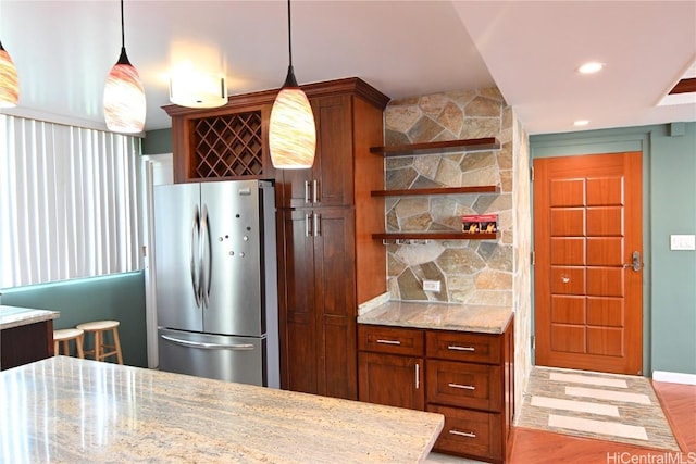 kitchen featuring hanging light fixtures, light stone counters, and stainless steel refrigerator