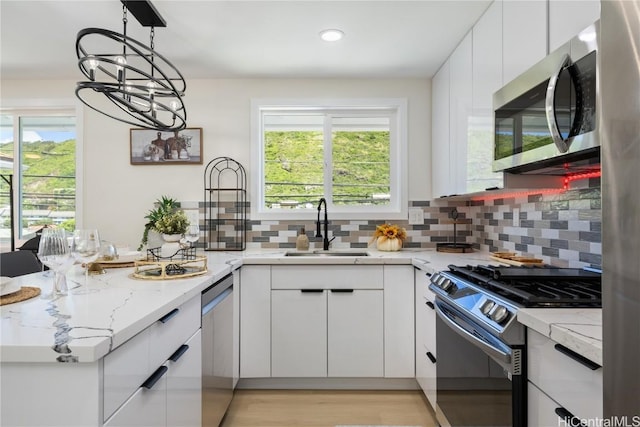 kitchen with sink, white cabinetry, decorative light fixtures, appliances with stainless steel finishes, and light stone countertops