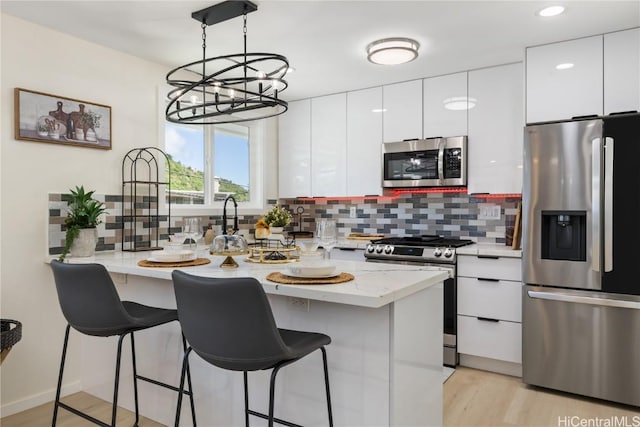 kitchen featuring tasteful backsplash, white cabinets, hanging light fixtures, stainless steel appliances, and light hardwood / wood-style flooring