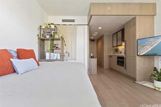 bedroom with beverage cooler, sink, and light hardwood / wood-style flooring