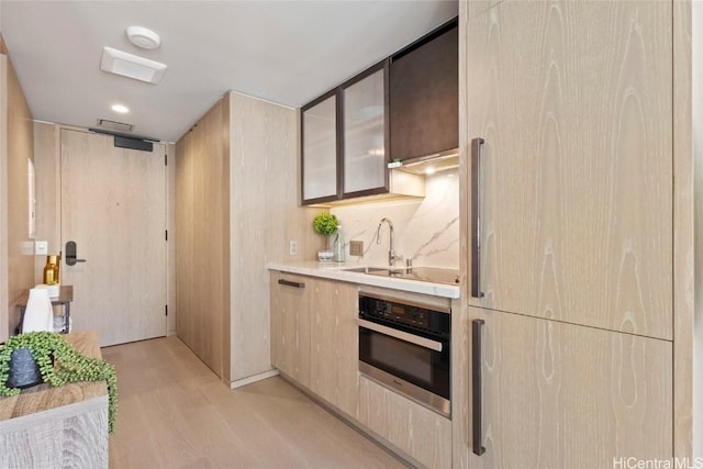 kitchen with tasteful backsplash, sink, light hardwood / wood-style floors, and oven