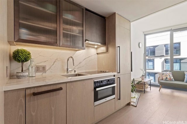 kitchen featuring tasteful backsplash, sink, wall oven, light hardwood / wood-style floors, and light stone countertops