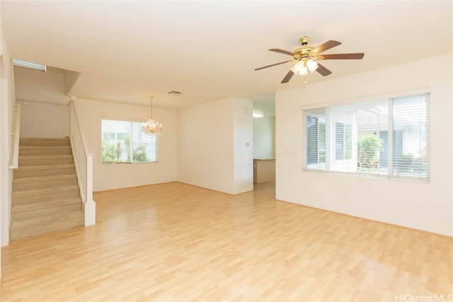 empty room with ceiling fan with notable chandelier, stairway, light wood-style floors, and visible vents