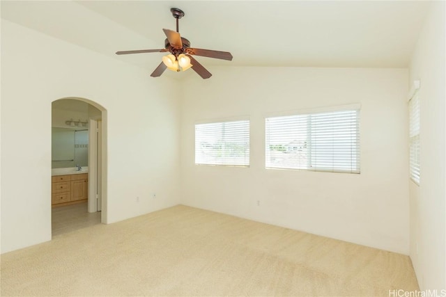 empty room with light colored carpet, lofted ceiling, arched walkways, a ceiling fan, and a sink