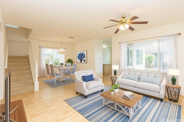 living room featuring visible vents, wood finished floors, stairs, and ceiling fan with notable chandelier