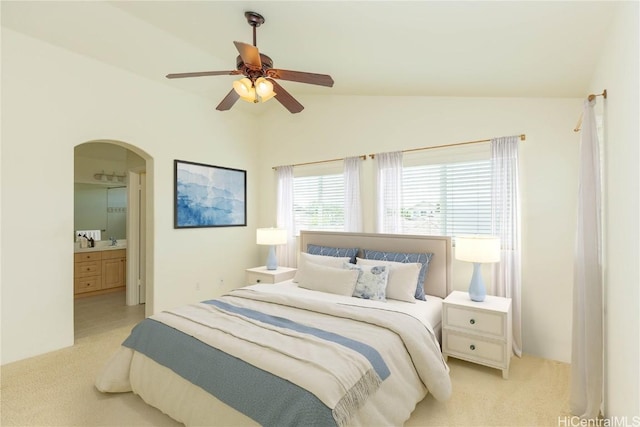 bedroom featuring connected bathroom, arched walkways, light carpet, and vaulted ceiling