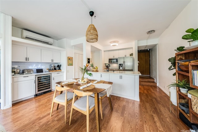 kitchen featuring a peninsula, wine cooler, light wood finished floors, a wall unit AC, and appliances with stainless steel finishes