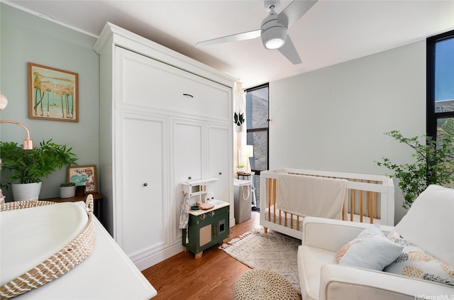 bedroom with a ceiling fan, a crib, floor to ceiling windows, and wood finished floors