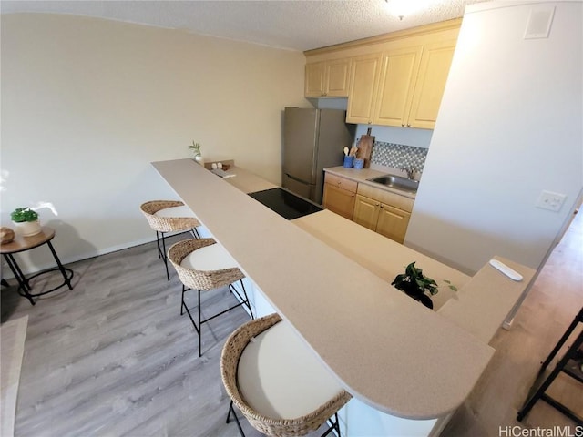 kitchen with a breakfast bar, sink, light hardwood / wood-style flooring, stainless steel refrigerator, and black electric stovetop