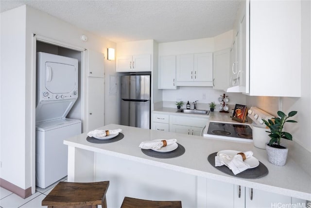 kitchen with stacked washer and clothes dryer, sink, stainless steel refrigerator, kitchen peninsula, and stove