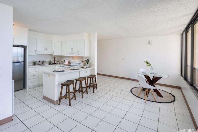 kitchen featuring a breakfast bar area, white cabinetry, a textured ceiling, electric range, and stainless steel refrigerator