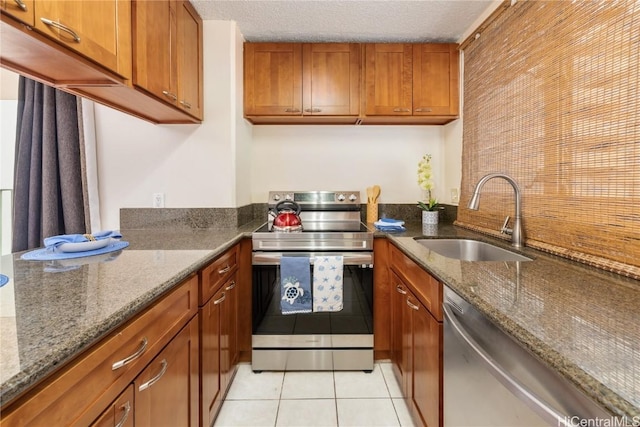 kitchen featuring light tile patterned flooring, sink, a textured ceiling, dark stone counters, and stainless steel appliances