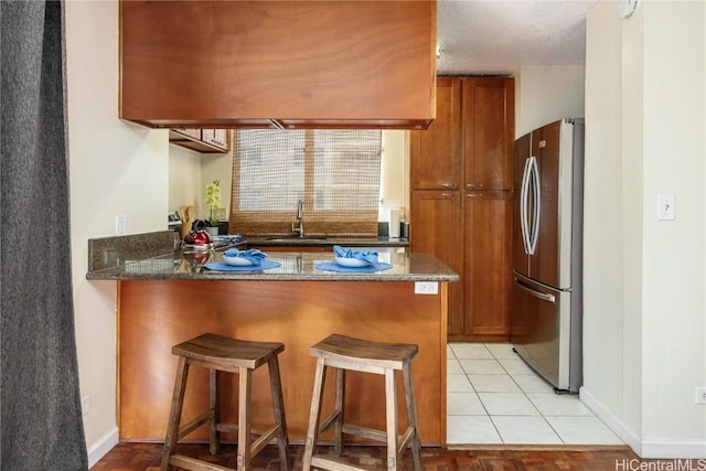 kitchen featuring stainless steel refrigerator, a breakfast bar area, dark stone counters, kitchen peninsula, and a textured ceiling