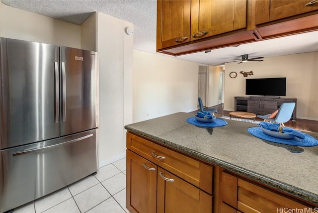 kitchen with light tile patterned flooring, stainless steel fridge, a textured ceiling, and dark stone countertops