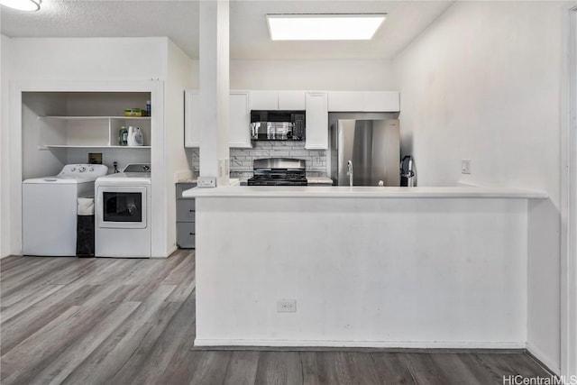 kitchen with black microwave, independent washer and dryer, freestanding refrigerator, light wood finished floors, and gas range oven