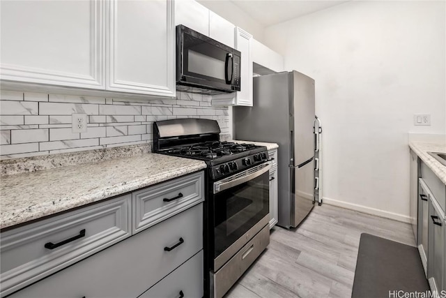 kitchen featuring stainless steel gas range oven, tasteful backsplash, gray cabinetry, light wood-style floors, and black microwave