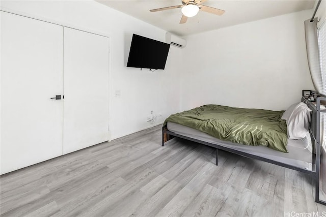 bedroom with ceiling fan, a closet, a wall unit AC, and light wood-style floors