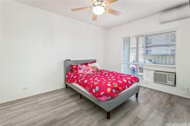 bedroom with a textured ceiling, wood finished floors, a ceiling fan, an AC wall unit, and a wall mounted air conditioner