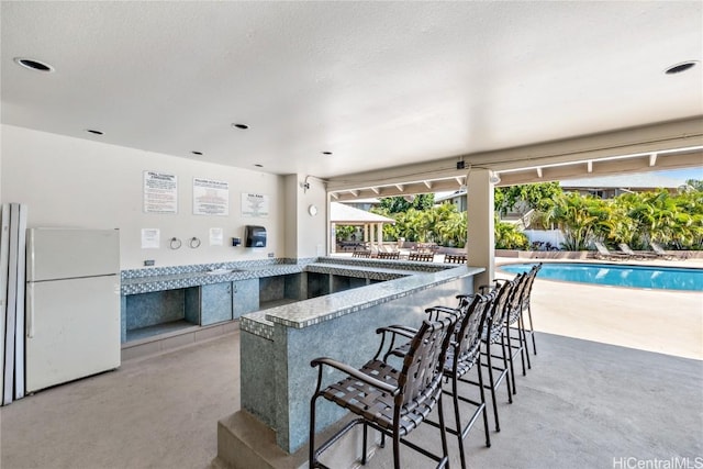 kitchen with concrete flooring, freestanding refrigerator, and a kitchen bar