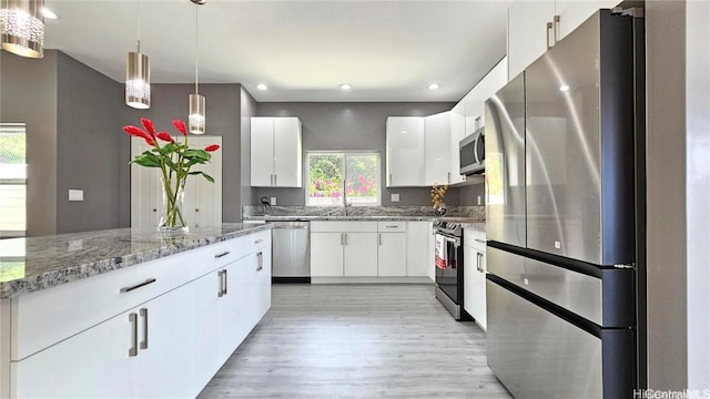 kitchen with white cabinetry, stainless steel appliances, light hardwood / wood-style floors, and hanging light fixtures