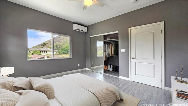 bedroom with hardwood / wood-style floors, a closet, an AC wall unit, and ceiling fan