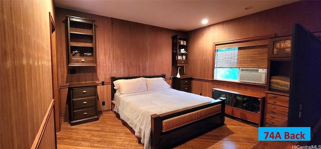 bedroom with cooling unit, light hardwood / wood-style flooring, and wood walls