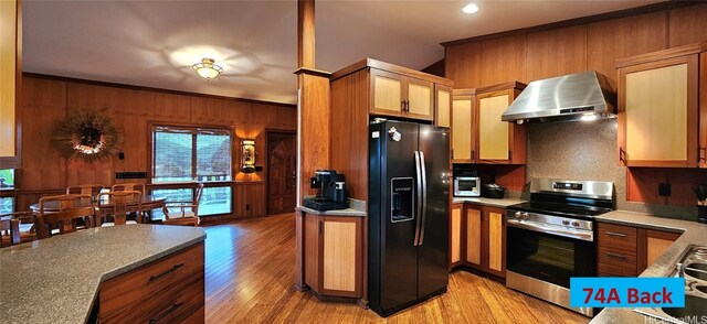 kitchen featuring wooden walls, light hardwood / wood-style floors, black fridge, wall chimney range hood, and electric stove