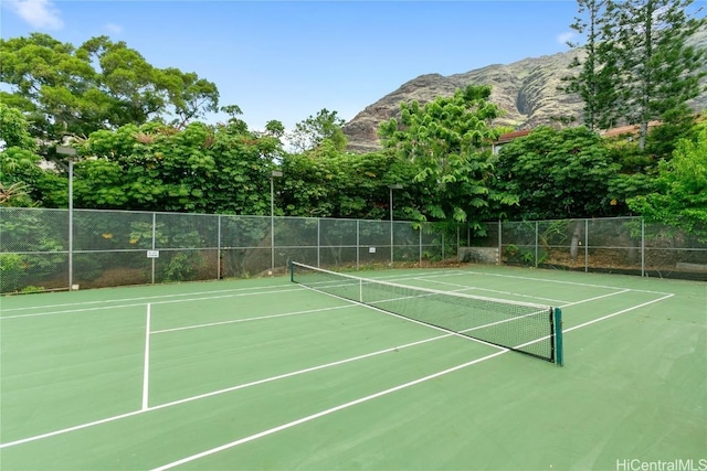 view of tennis court featuring a mountain view and fence