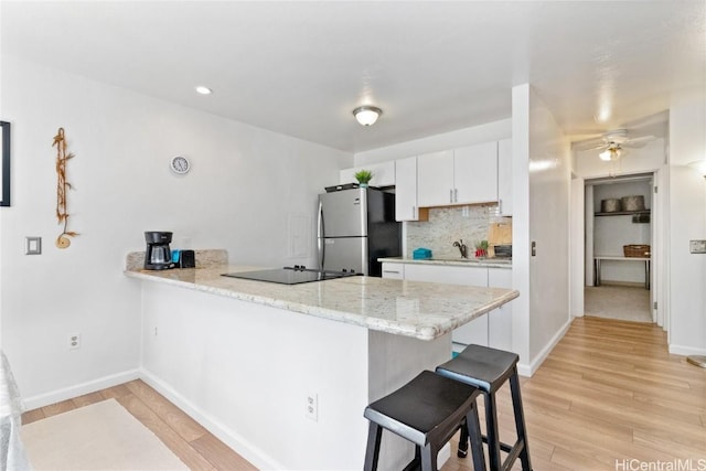 kitchen featuring a peninsula, white cabinetry, light wood-style floors, freestanding refrigerator, and a kitchen bar