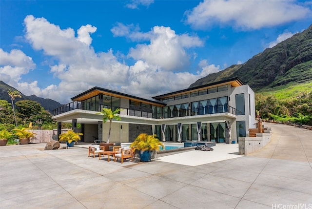 back of property with a mountain view, a patio, an outdoor pool, and a balcony