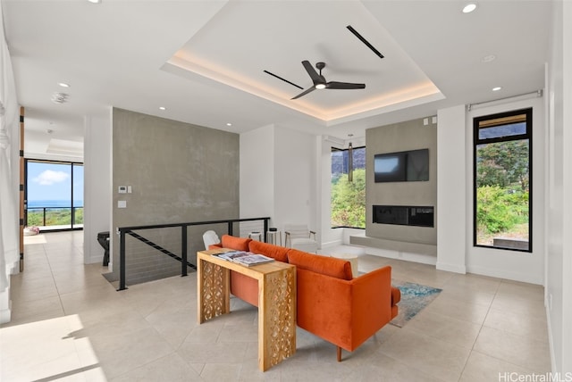 living room with baseboards, a fireplace, ceiling fan, a raised ceiling, and light tile patterned floors
