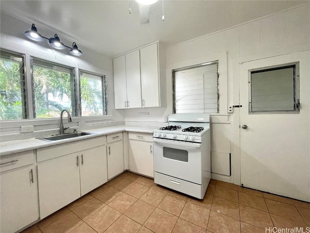 kitchen with white gas stove, white cabinetry, light tile patterned floors, and sink