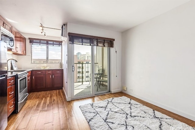 kitchen featuring stainless steel appliances, rail lighting, light stone counters, and light hardwood / wood-style flooring