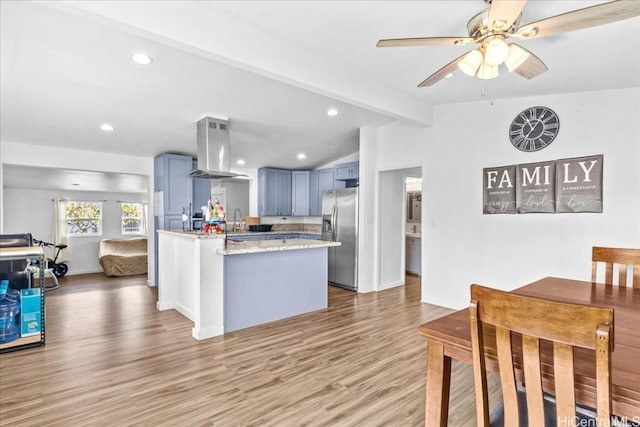 kitchen with vaulted ceiling with beams, light wood-style floors, island range hood, stainless steel fridge, and a peninsula