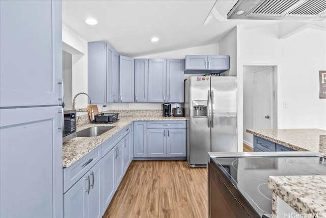 kitchen featuring light stone counters, stainless steel appliances, lofted ceiling, light wood-style floors, and a sink