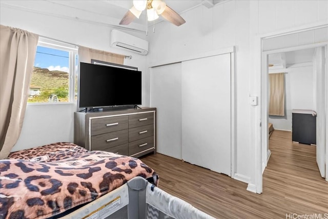 bedroom with ceiling fan, a closet, wood finished floors, and a wall mounted AC