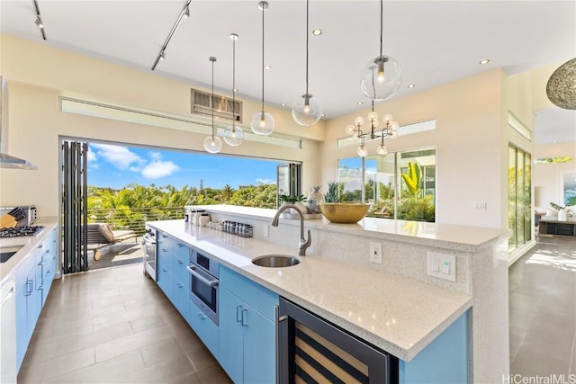 kitchen with sink, wine cooler, light stone countertops, a center island with sink, and decorative light fixtures