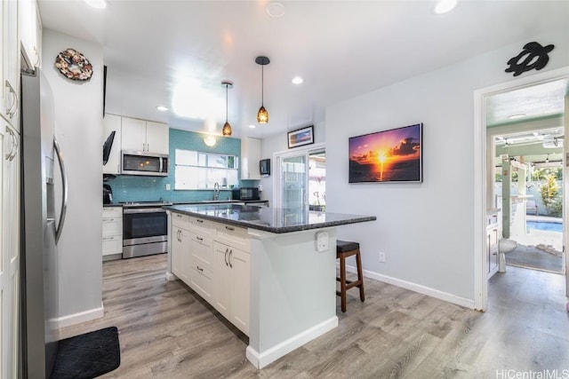 kitchen with decorative light fixtures, light hardwood / wood-style flooring, a kitchen island, stainless steel appliances, and white cabinets