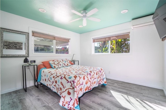 bedroom with hardwood / wood-style floors, a wall mounted AC, and ceiling fan