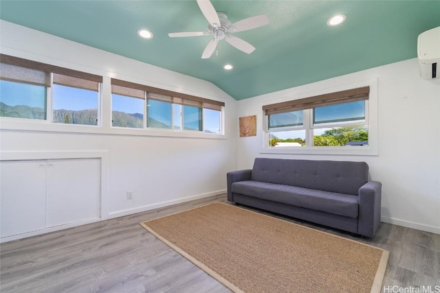 living area with ceiling fan, an AC wall unit, lofted ceiling, and light wood-type flooring