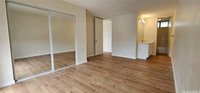 unfurnished bedroom with a closet, sink, light wood-type flooring, and ensuite bath