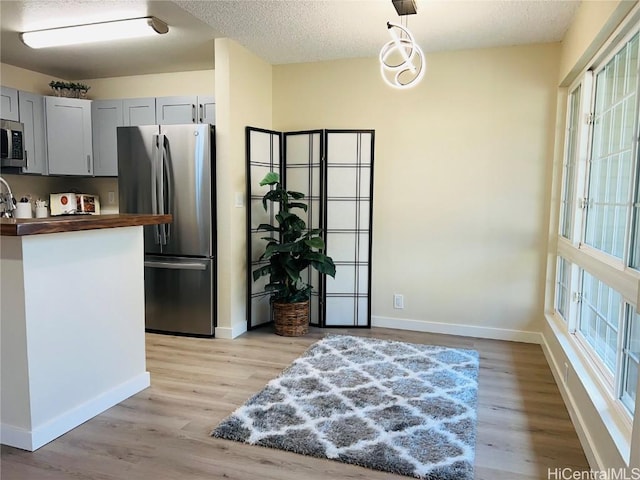 kitchen with gray cabinets, decorative light fixtures, butcher block counters, light hardwood / wood-style floors, and stainless steel appliances